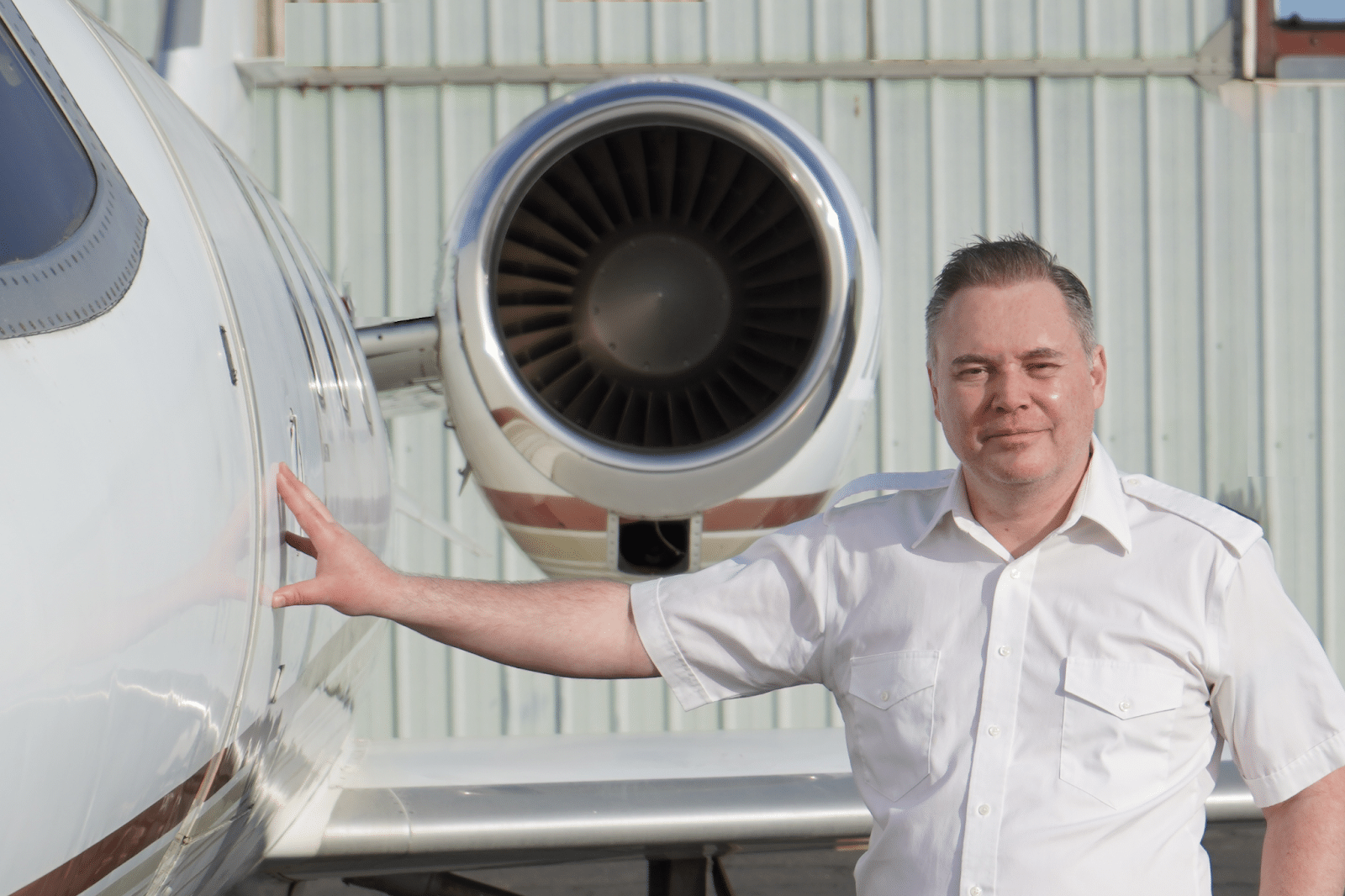 En mand i en hvid skjorte står ved siden af et slankt privatfly med den ene hånd afslappet hvilende på flyet. I nærheden skinner den raffinerede silhuet af Sierra Plus-teknologi inde fra den synlige jetmotor. Nicki Repenning – CEO, Meridian